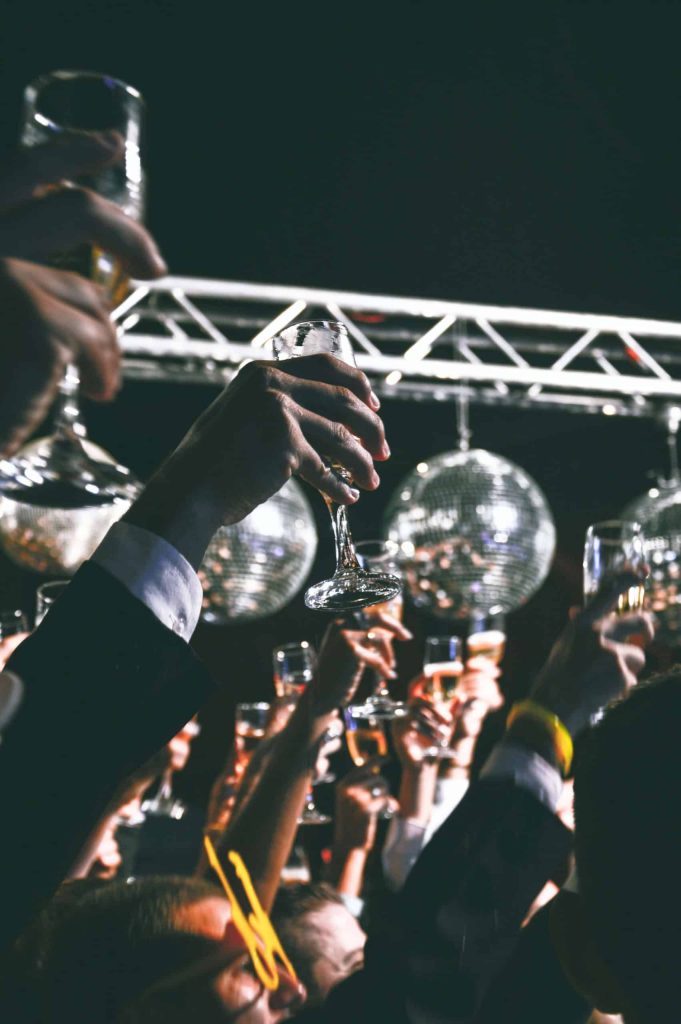 an imgae of weddings guest beneath disco balls raising glasses